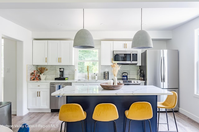 kitchen featuring a center island, sink, stainless steel appliances, decorative light fixtures, and white cabinets