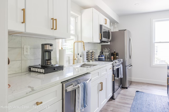 kitchen featuring light stone countertops, stainless steel appliances, white cabinetry, and plenty of natural light