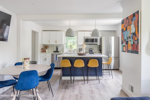 kitchen with pendant lighting, backsplash, light wood-type flooring, appliances with stainless steel finishes, and white cabinetry