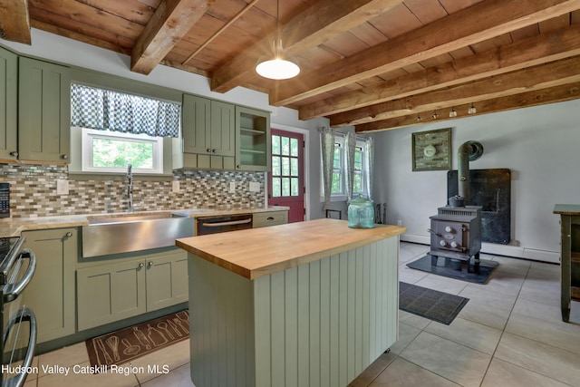 kitchen featuring a wood stove, sink, green cabinetry, a wealth of natural light, and butcher block countertops