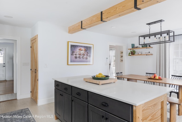 kitchen featuring open shelves, light countertops, baseboards, dark cabinets, and a kitchen island