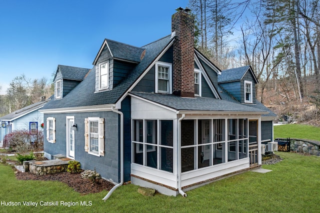 rear view of property featuring a chimney, a sunroom, a yard, and roof with shingles