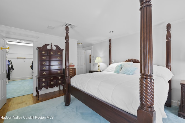 bedroom with crown molding, a spacious closet, wood finished floors, and visible vents
