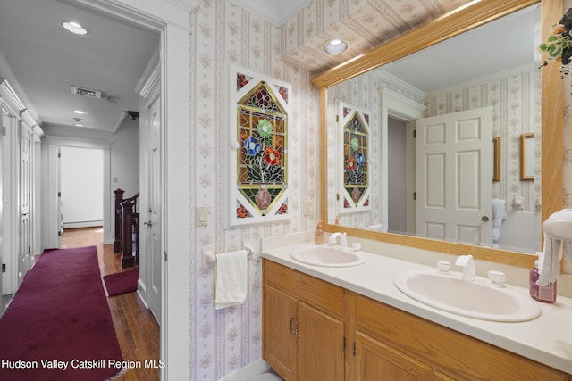 bathroom featuring crown molding, a sink, wood finished floors, and wallpapered walls