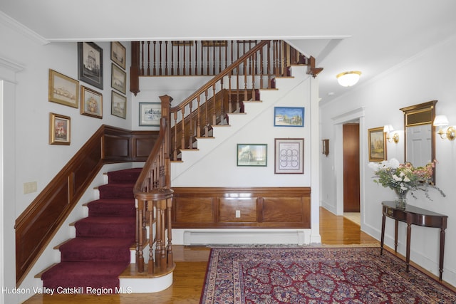 stairway with wood finished floors, crown molding, and a baseboard heating unit