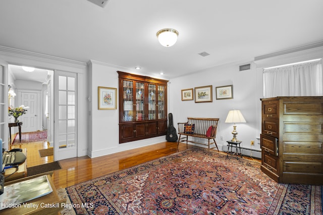 sitting room featuring visible vents, ornamental molding, wood finished floors, baseboards, and baseboard heating