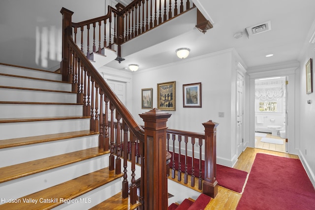 stairway featuring baseboards, visible vents, ornamental molding, and wood finished floors