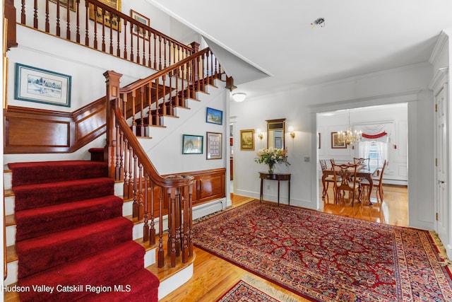 entryway with an inviting chandelier, ornamental molding, wood finished floors, stairway, and a baseboard radiator