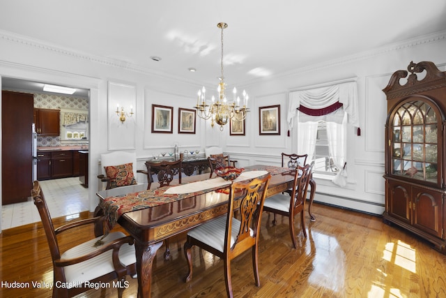 dining area with a decorative wall, light wood-style floors, an inviting chandelier, and a baseboard radiator