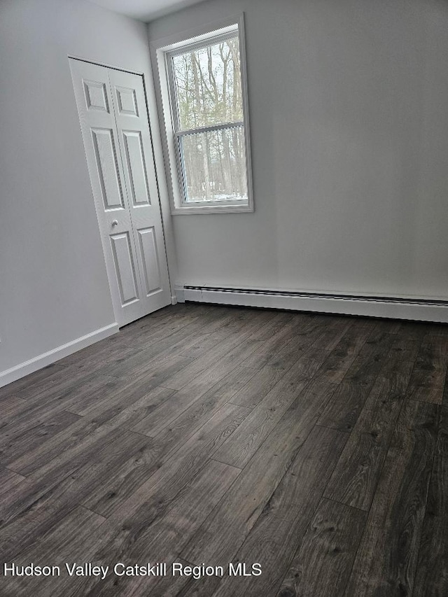 empty room featuring baseboards, baseboard heating, and dark wood-style floors