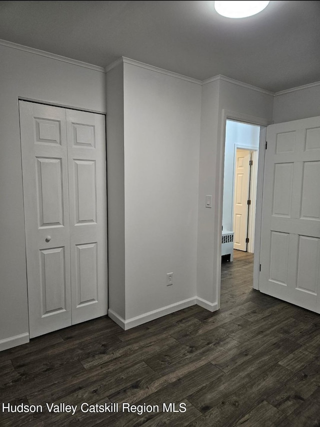 unfurnished bedroom with a closet, baseboards, dark wood-style floors, and crown molding