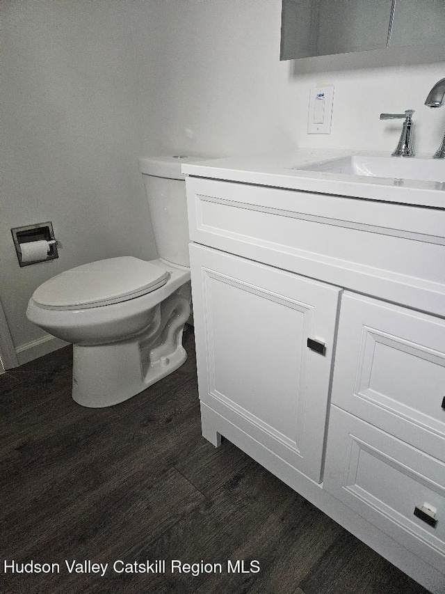 half bathroom with toilet, wood finished floors, and vanity