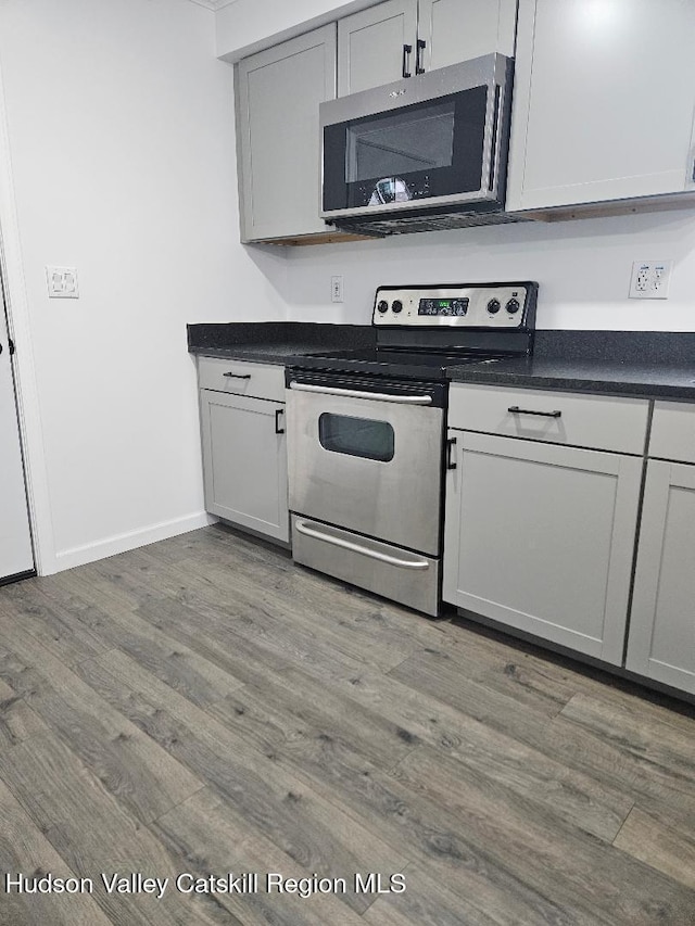 kitchen with stainless steel appliances, baseboards, dark countertops, and wood finished floors