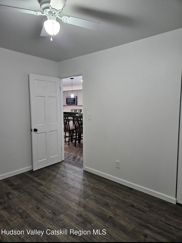 spare room featuring baseboards, ceiling fan, and dark wood-style flooring