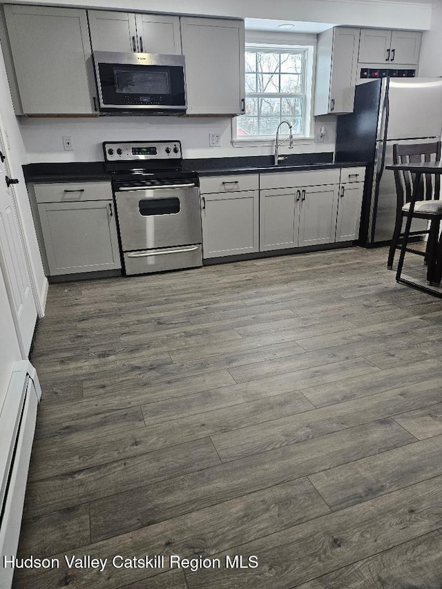 kitchen with dark wood-type flooring, a sink, a baseboard heating unit, dark countertops, and appliances with stainless steel finishes