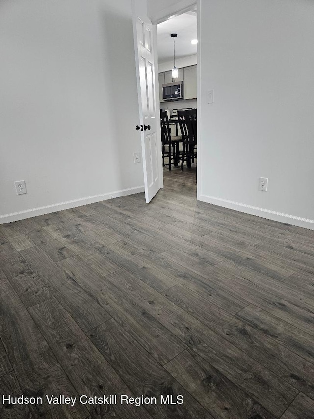 unfurnished room featuring baseboards and dark wood-style flooring