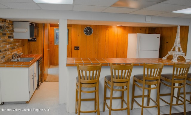 kitchen with tile counters, white fridge, a drop ceiling, and sink