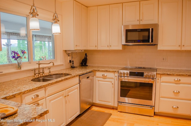 kitchen featuring appliances with stainless steel finishes, sink, white cabinets, light hardwood / wood-style floors, and hanging light fixtures