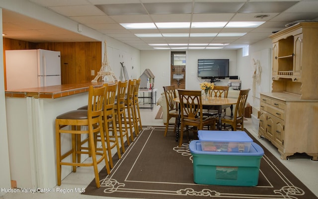 carpeted dining area with a drop ceiling and wooden walls