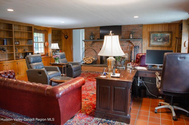 tiled living room featuring built in features, wooden walls, and a brick fireplace