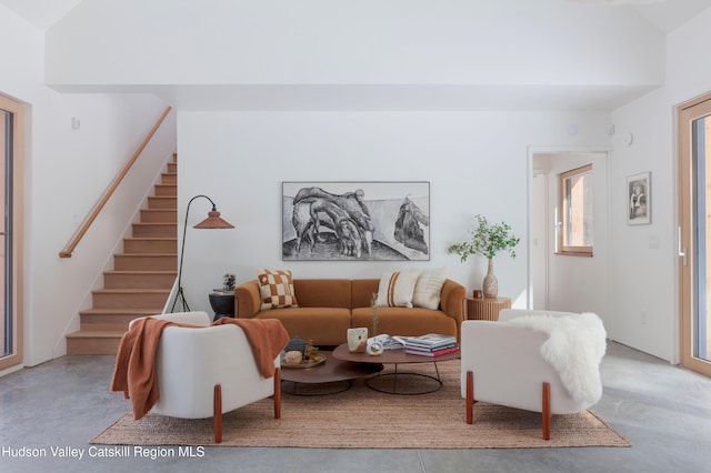 living room featuring lofted ceiling, stairs, and concrete flooring