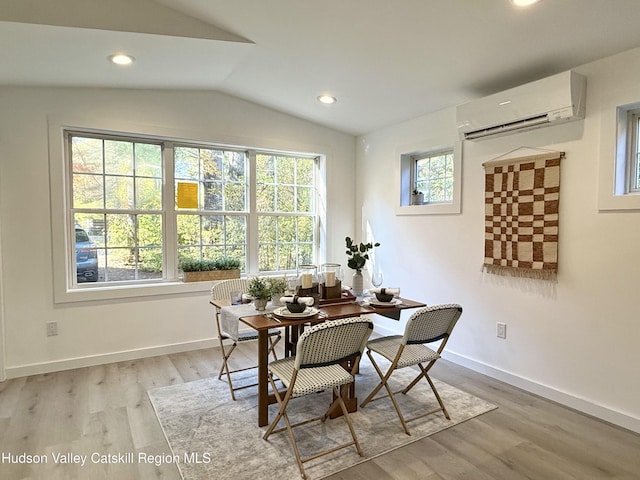 dining space with vaulted ceiling, light hardwood / wood-style flooring, a wall unit AC, and a wealth of natural light