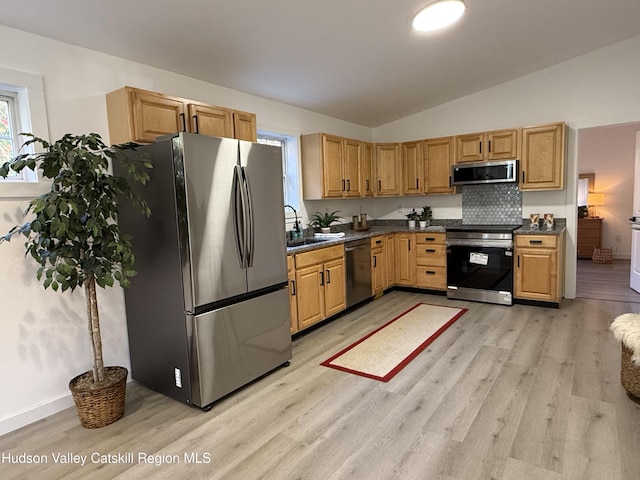 kitchen featuring sink, vaulted ceiling, appliances with stainless steel finishes, tasteful backsplash, and light hardwood / wood-style floors