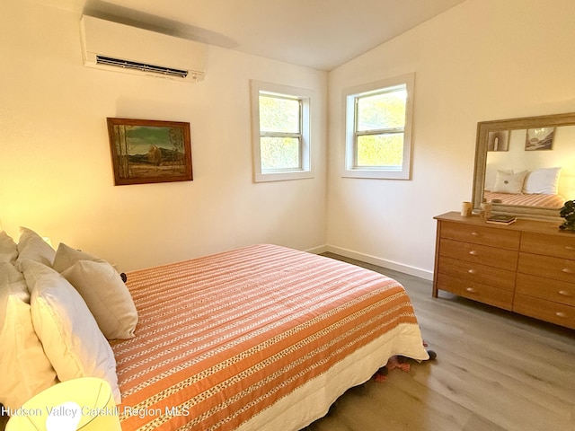 bedroom with vaulted ceiling, hardwood / wood-style floors, and a wall mounted air conditioner