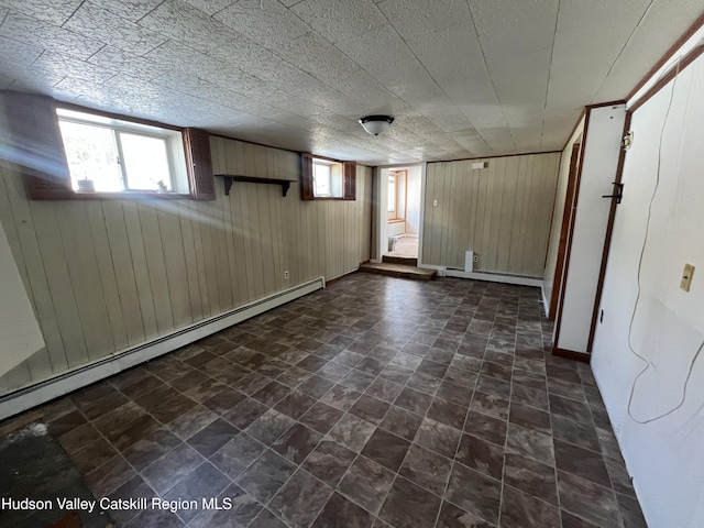 basement featuring wooden walls and a baseboard heating unit