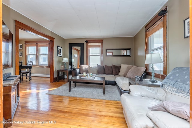 living room with a baseboard heating unit, light wood-style floors, and a healthy amount of sunlight