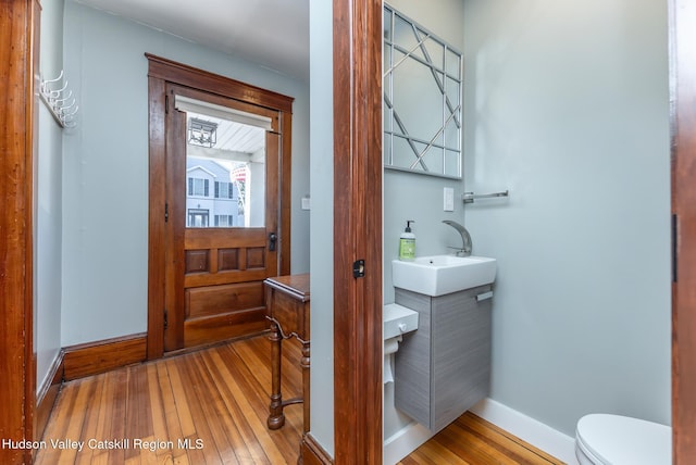 half bathroom featuring toilet, vanity, baseboards, and hardwood / wood-style floors