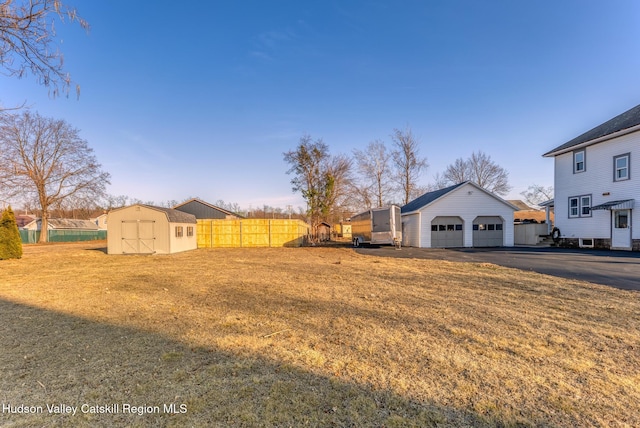 view of yard featuring a detached garage, an outbuilding, and fence