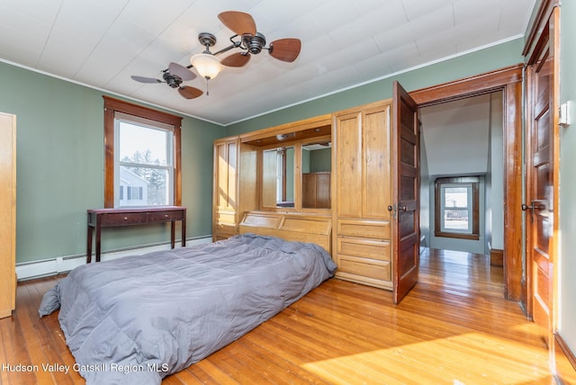 bedroom featuring a baseboard heating unit, baseboards, ornamental molding, and light wood finished floors