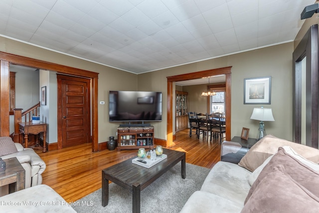 living room with wood finished floors, an inviting chandelier, crown molding, baseboards, and stairs