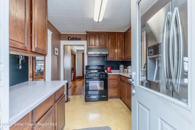 kitchen featuring black gas range, brown cabinetry, stainless steel fridge, and under cabinet range hood