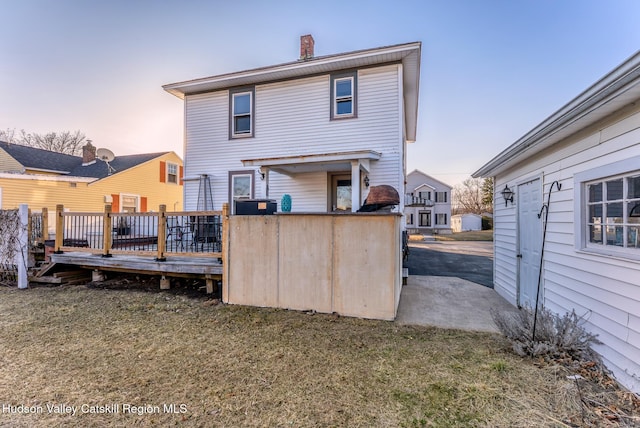 back of property featuring a lawn, a chimney, and a deck