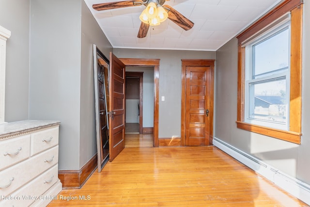 unfurnished bedroom featuring a baseboard heating unit, light wood-style floors, and baseboards