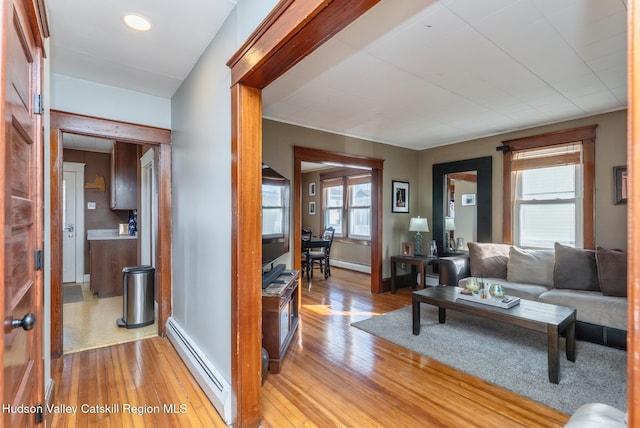 living area with a baseboard heating unit, plenty of natural light, and light wood finished floors