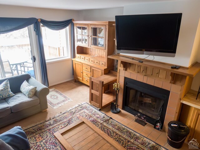 living room featuring a tile fireplace, baseboards, and light colored carpet