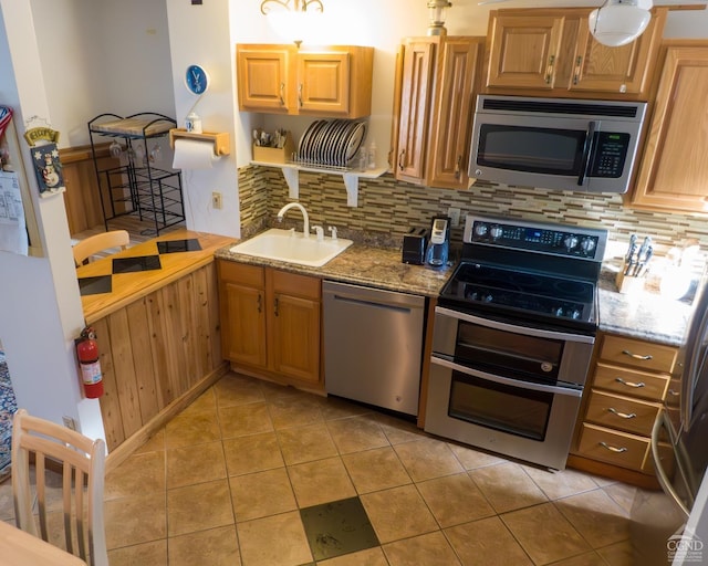 kitchen featuring stainless steel appliances, a sink, backsplash, light stone countertops, and light tile patterned floors