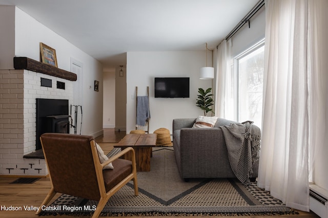 living room featuring baseboard heating, a wood stove, and hardwood / wood-style floors