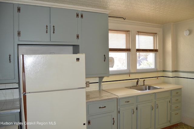 kitchen featuring light countertops, freestanding refrigerator, a textured ceiling, tile walls, and a sink