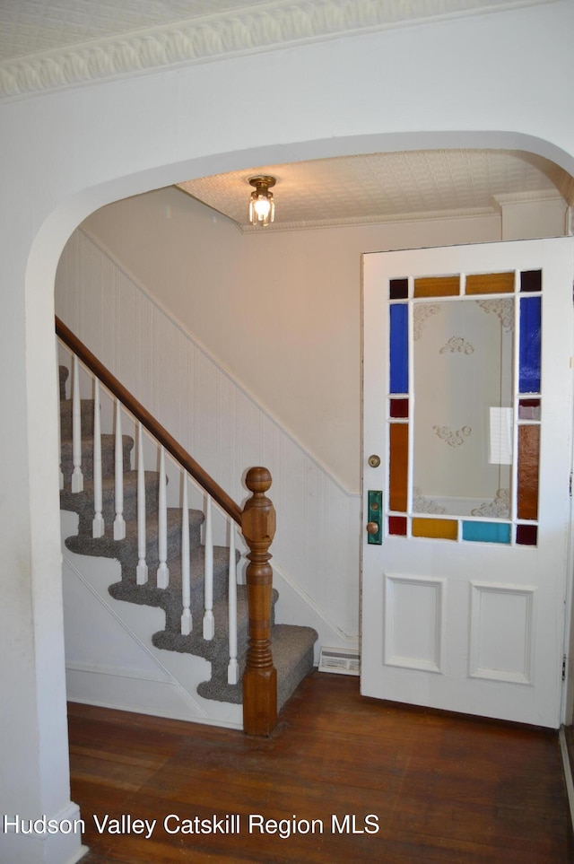 foyer entrance featuring stairs, wood finished floors, a wainscoted wall, and arched walkways