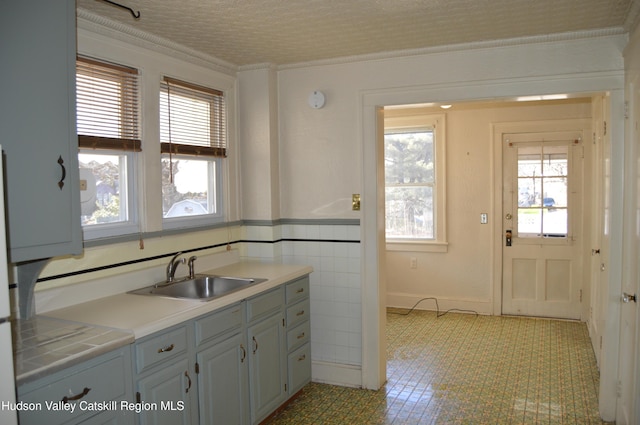 kitchen with a wainscoted wall, light countertops, ornamental molding, tile walls, and a sink