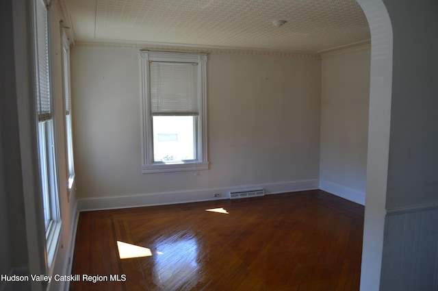 empty room featuring visible vents, crown molding, baseboards, wood finished floors, and arched walkways