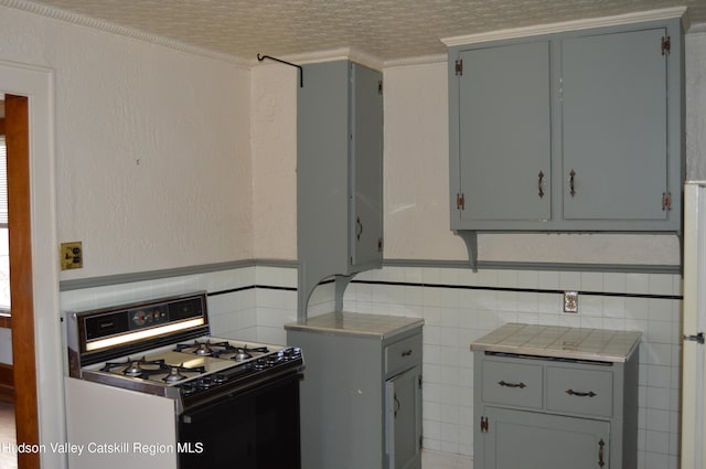 kitchen with gray cabinetry, range with gas cooktop, tile walls, tile counters, and a textured wall