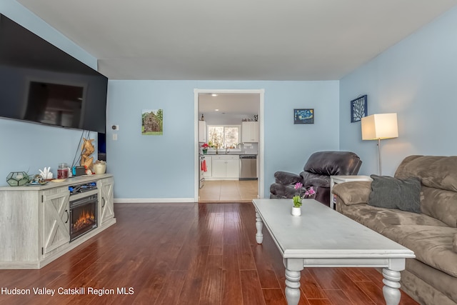 living room featuring dark wood-style floors, a lit fireplace, and baseboards