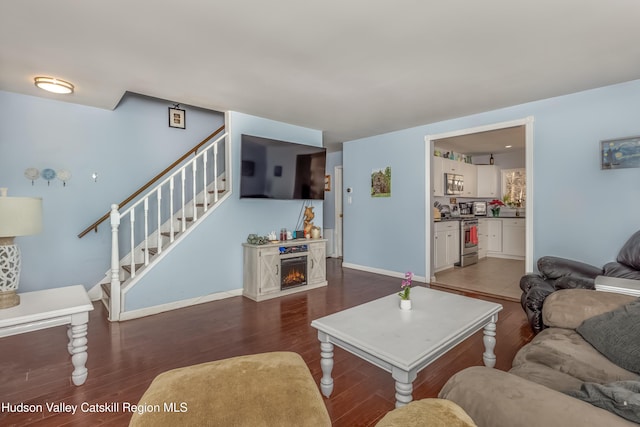 living room with a warm lit fireplace, stairway, dark wood-style floors, and baseboards