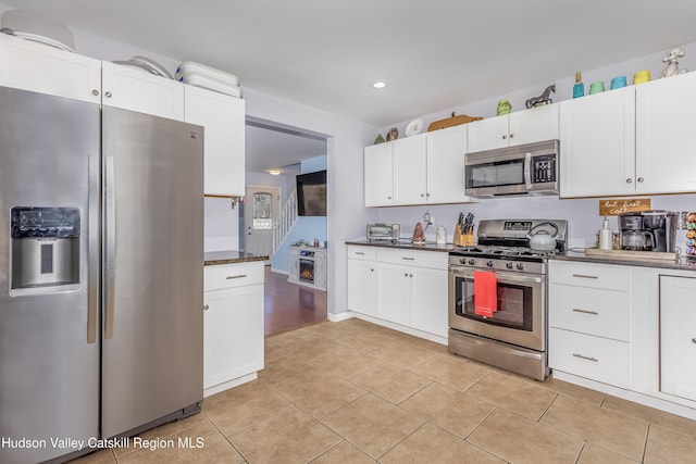 kitchen featuring light tile patterned floors, appliances with stainless steel finishes, dark stone counters, and white cabinetry