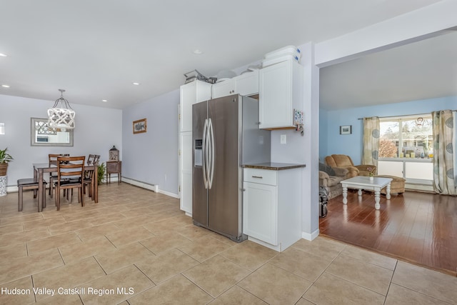 kitchen featuring light tile patterned floors, stainless steel fridge, dark countertops, hanging light fixtures, and white cabinetry